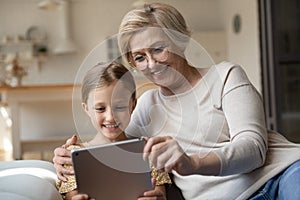 Smiling granny and small granddaughter use tablet