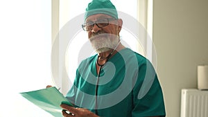 Smiling gray-bearded doctor holding a file with the patient`s medical history. Medicine and healthcare concept