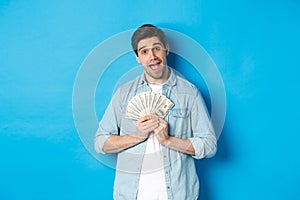 Smiling greedy guy hugging money and smiling, unwilling to share, standing over blue background