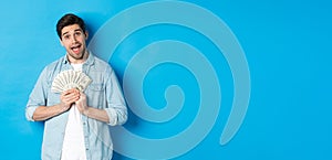 Smiling greedy guy hugging money and smiling, unwilling to share, standing over blue background