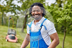 Smiling in Green Fields: Afro-American Groundskeeper Radiates Joy Amidst the Lawn with Lawnmower in Background