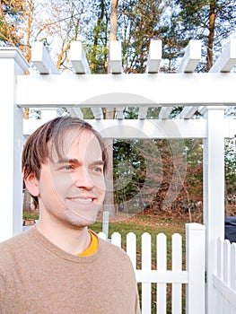 Smiling in Greeting Standing Before White Picket Fence on Autumn Day, Casually Dressed