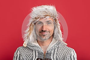 smiling grizzled man in sweater and earflap on red background, portrait