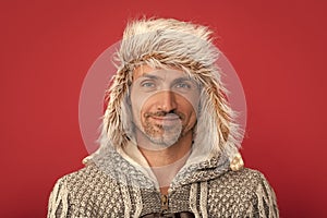 smiling grizzled man in sweater and earflap on red background, portrait