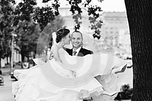 Smiling groom carries bride in magnificent dress on his arms