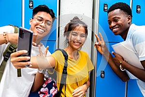 Smiling group of multiracial teen friends taking a selfie in high school corridor