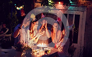 Smiling group of young friends having  birthday party in the club with cake and candles at night.  Party, fun, birthday concept