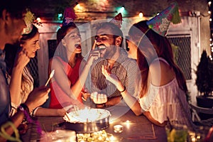 Smiling group of young friends having  birthday party in the club with cake and candles at night.  Party, fun, birthday concept