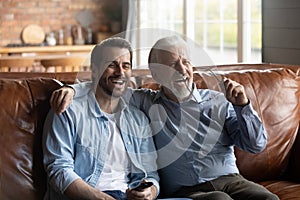 Smiling grownup son and old father watch TV together