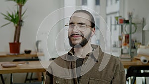 Smiling guy with beard and glasses shakes head at office