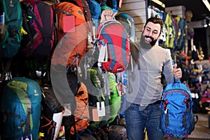 Smiling guy customer examining rucksacks in store