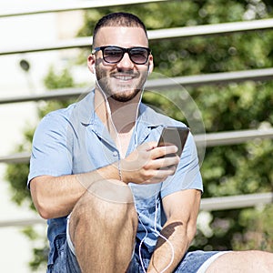 Smiling guy with earphones using phone