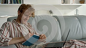 Smiling guy elearning home on weekend closeup. Ginger student work making notes