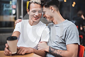 Smiling guy embracing cheerful friend at table