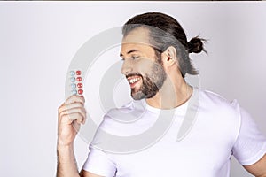 Smiling guy holding pills in his hands. A man in a white shirt watching at dietary supplements on a white background