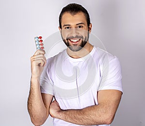 Smiling guy holding pills in his hands. Vitamin C. Man in white shirt with red and blue tablets on a white background