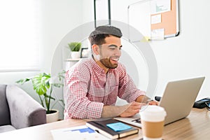 Smiling guy at the office is typing on his laptop