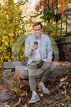 Smiling guy with a phone in casual clothes in the autumn park