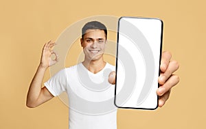 Smiling guy showing white empty smartphone screen and ok sign