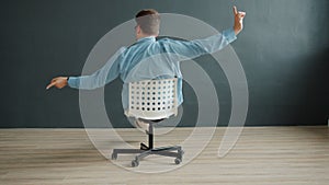 Smiling guy spinning on office chair pointing at camera on dark gray background