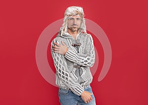 smiling guy in sweater and earflap hat on red background, winter fashion