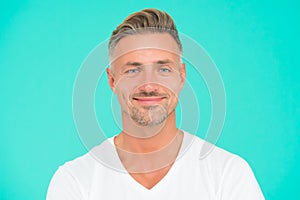 Smiling guy with trendy hairstyle has colored graying hair and groomed face on turquoise background, personal care