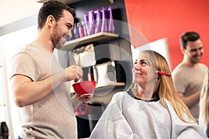 Smiling hair styling with his blonde costumer at beauty salon