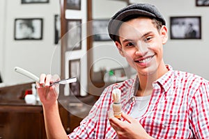 Smiling hairdresser holding razor and shaving brush