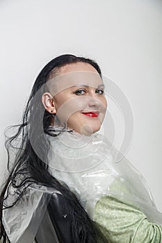 Smiling with half shaved head brunette woman with bright makeup in barber chair.