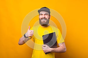 Smiling handsome bearded man showing thumb up and holding laptop