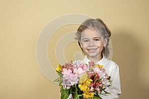 smiling handsome boy holds out a bouquet of colorful flowers on yellow background. happy child gives a bouquet of