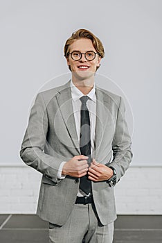 smiling handsome businessman touching jacket and looking at camera