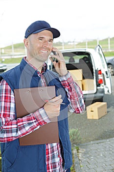 Smiling handsome delivery man holding box and making call