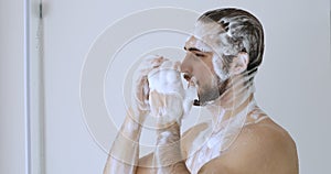 Smiling handsome groomed guy washing scalp hair in shower.
