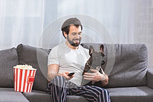 smiling handsome loner sitting with bulldog on sofa in living