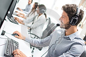 Smiling handsome male customer support phone operator with headset working in call centre