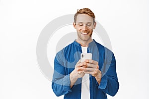 Smiling handsome man looking at his phone screen, reading or watching video on smartphone app, staring pleased at