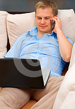 Smiling handsome man with phone lying at couch