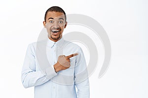 Smiling handsome man pointing right, showing direction, demonstarting promo, standing over white background
