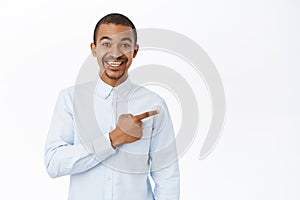 Smiling handsome man pointing right, showing direction, demonstarting promo, standing over white background