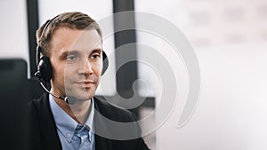 A smiling handsome man sitting in a customer service department office with headset working in call centre