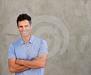 Smiling handsome man standing by wall with arms crossed