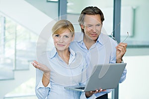 Smiling handsome, mature businessman and confident businesswoman, working on laptop computer in modern office building