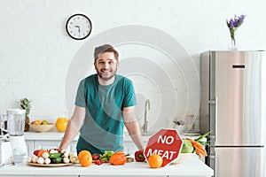 smiling handsome vegan man standing near kitchen counter with vegetables and no