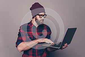 Smiling handsome young man in cap and glasses holding modern laptop