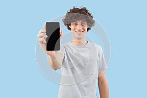 Smiling and handsome, the young man showing the blank screen of his smartphone to the camera, while looking into the camera with