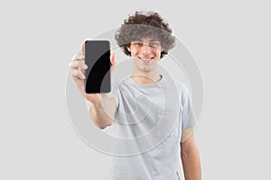 Smiling and handsome, the young man showing the blank screen of his smartphone to the camera, while looking into the camera with