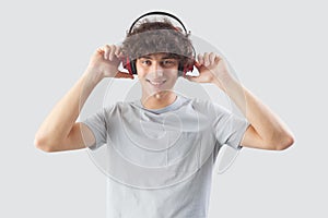 Smiling and handsome, the young man wears headphones and is isolated against a gray background. He looks at the camera with his