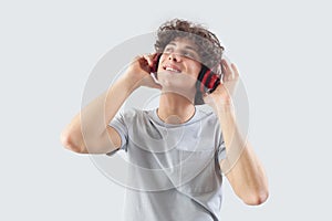 Smiling and handsome, the young man wears headphones and is isolated against a gray background. He looks to the side with his blue