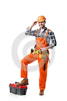 Smiling handyman in orange overall and hard hat leaning on tool box